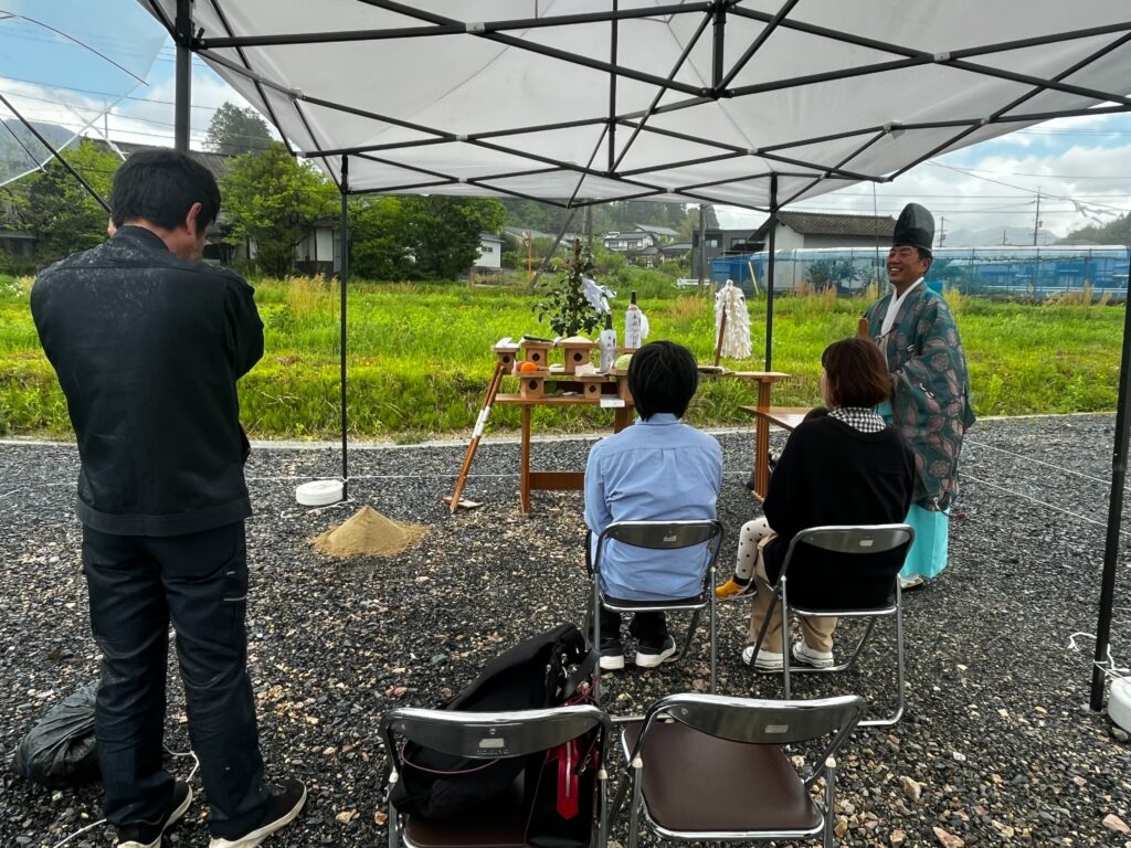 Shooter to note: An outdoor Shinto-style ceremony under a white canopy, with a priest in traditional teal robes at a small altar of offerings.