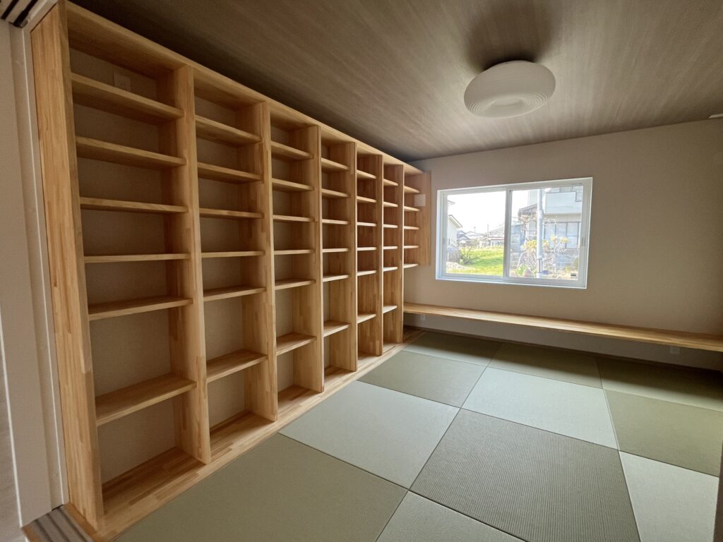 Empty wooden shelving units line a wall in a bright room with a large window and a round ceiling light.