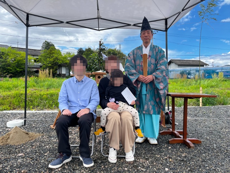 Family posing under a canopy for a ceremony; a priest in traditional robes stands nearby outdoors.