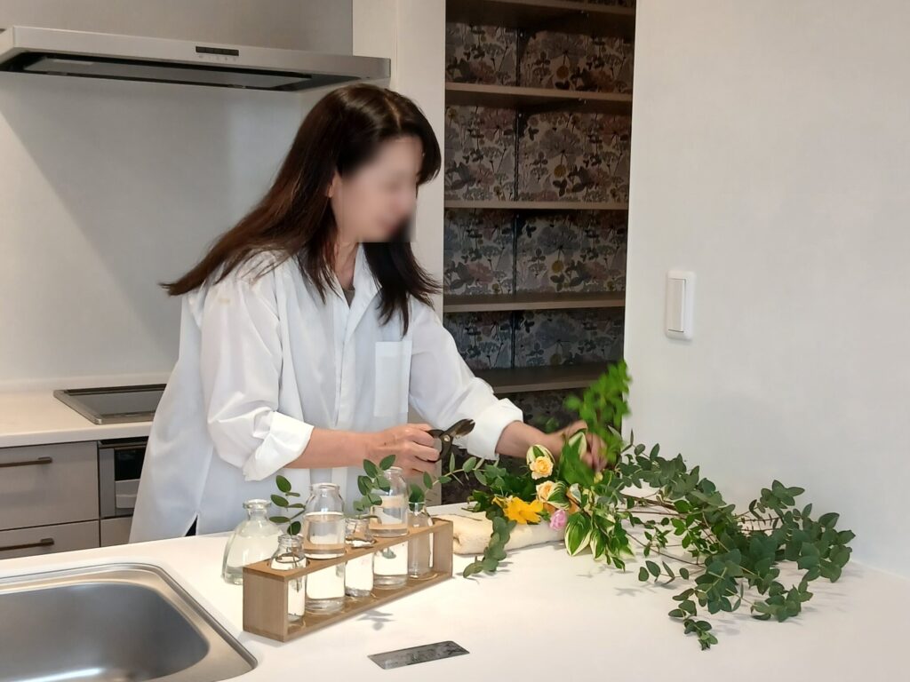 Person in a white coat arranging yellow flowers and green foliage on a white kitchen island.