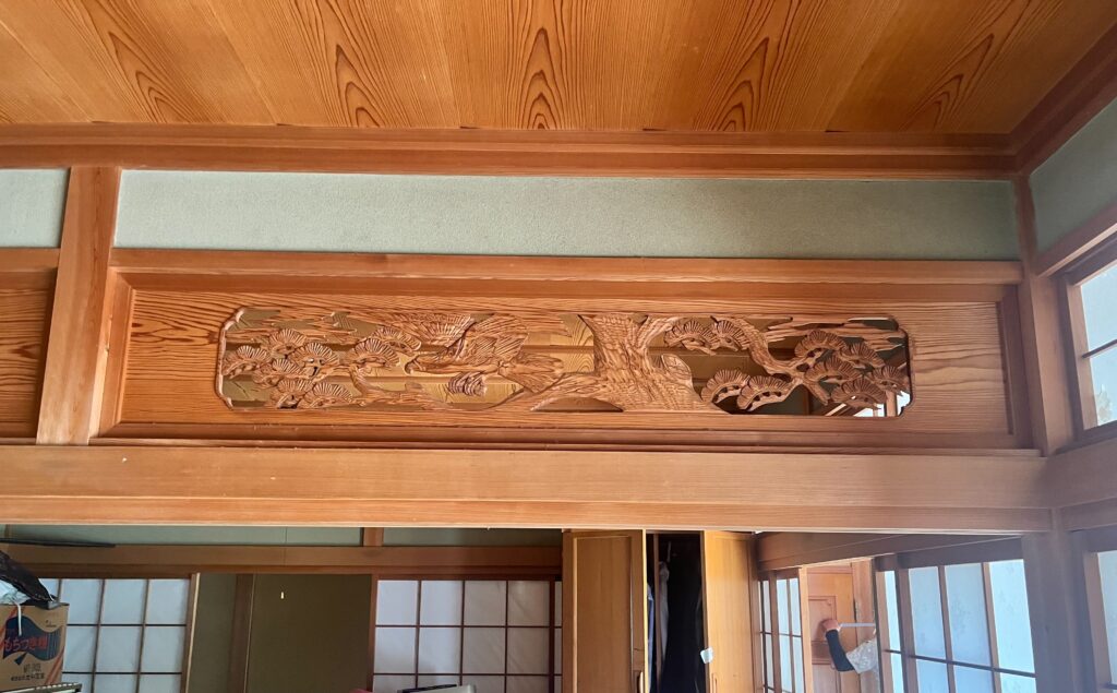 Carved wooden panel with cranes and pine motif above a doorway in a traditional wooden interior