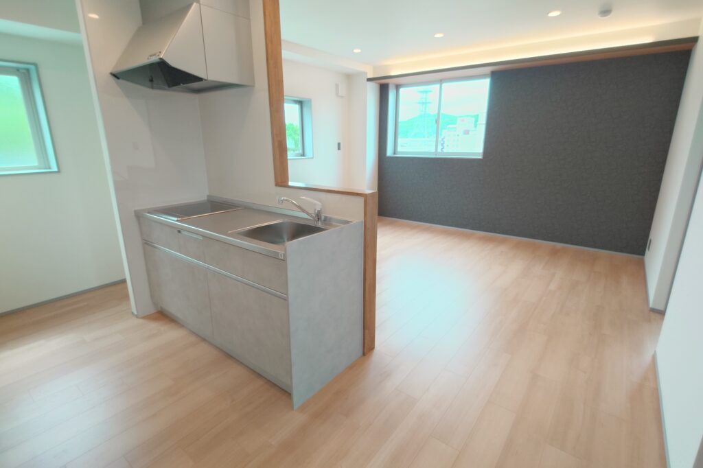 20260615_095157402-1 | 津山で注文住宅・デザイン住宅をちょうどいい価格で建てる工務店 |住宅産業センター Modern kitchen with a gray island, double sink, and stainless steel countertop, open to a living area with large windows.