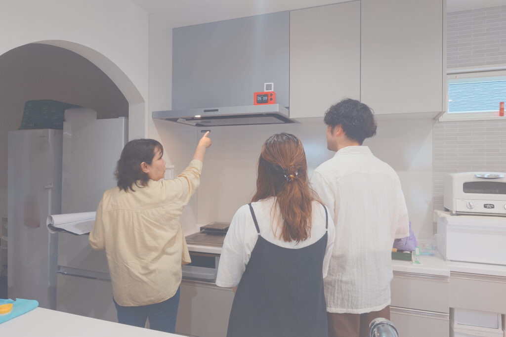 Three people gathered in a modern kitchen, with one pointing toward the range hood above the stove as the others look on.