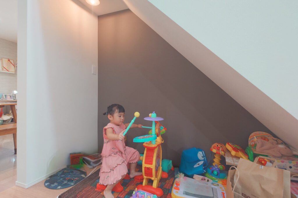 Young girl in a pink dress playing with a colorful toy activity center in a cluttered playroom.